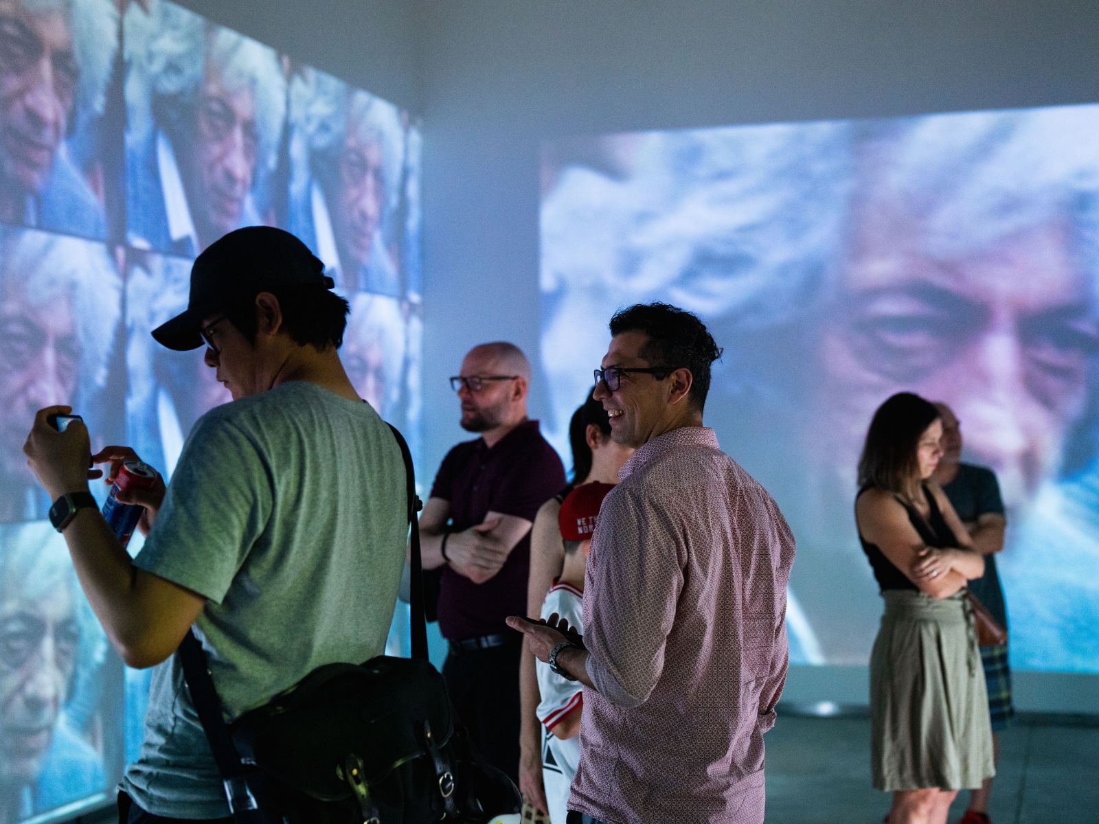 Medium-long shot of spectators observing a video projection of a man with grey hair.